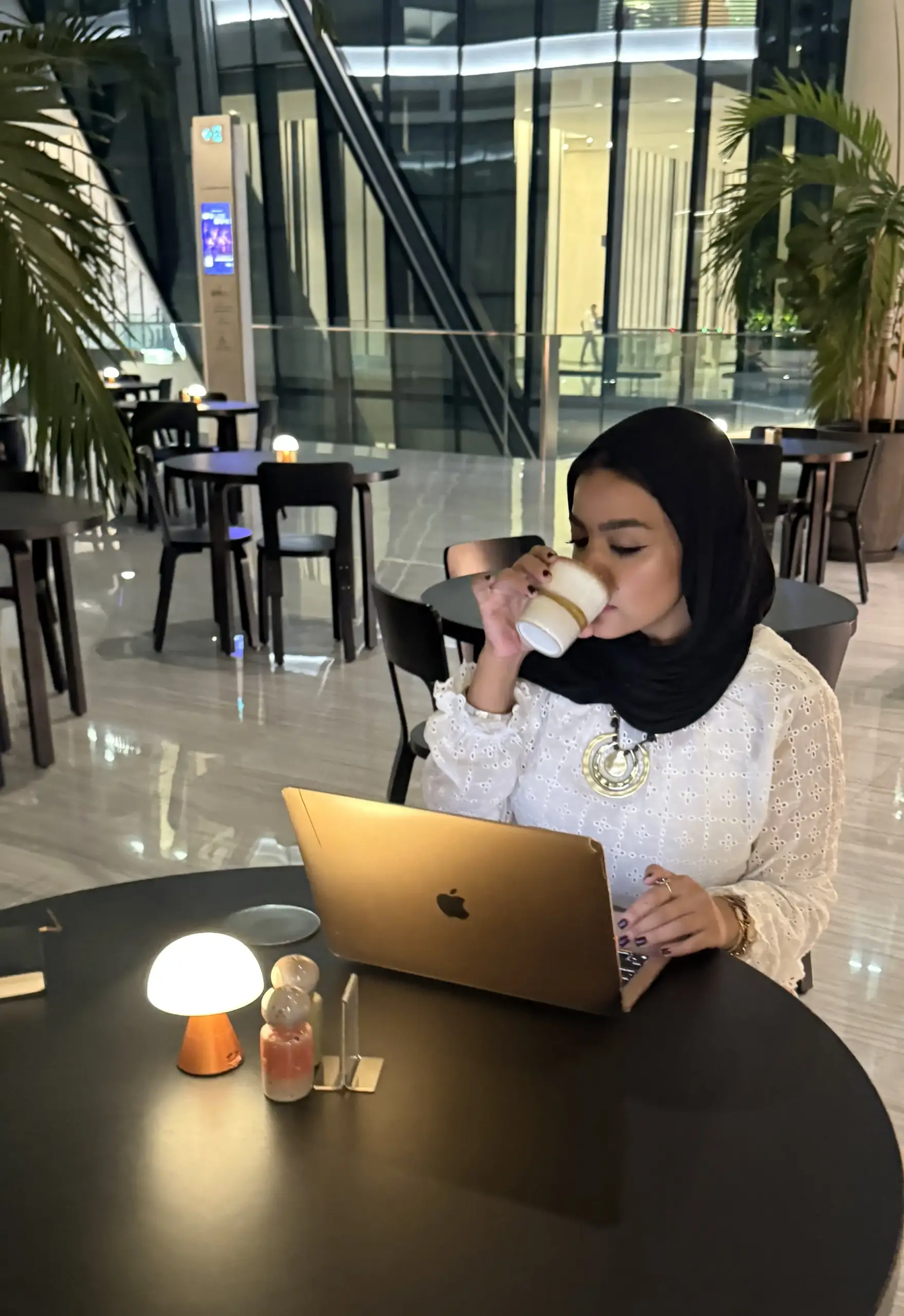 سيدة تعمل على لابتوب وتحتسي القهوة في مقهى عصري—مشهد يوضح الأعراض الصحية والقهوة مثل الأرق والخفقان عند الإفراط.