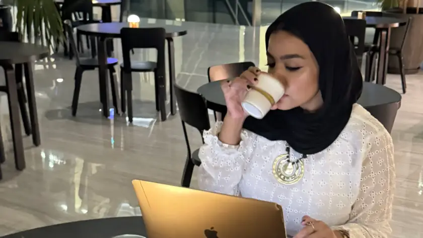 سيدة تعمل على لابتوب وتحتسي القهوة في مقهى عصري—مشهد يوضح الأعراض الصحية والقهوة مثل الأرق والخفقان عند الإفراط.