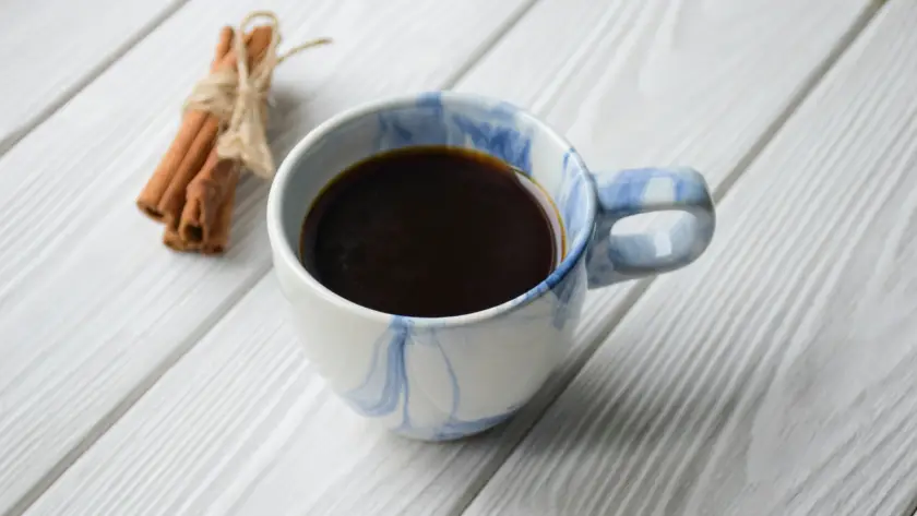 فنجان قهوة سوداء مع عيدان قرفة على سطح خشبي—وصفة القهوة العلاجية بالقرفة.